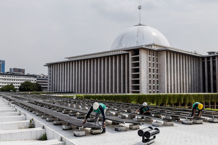 Pekerja memasang panel surya di dekat sebuah masjid.
